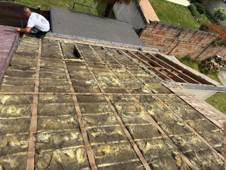Isolant posé entre les chevrons d'une toiture découverte, couvreur au travail en haut du pan — M. Simonard, couvreur en Seine-et-Marne